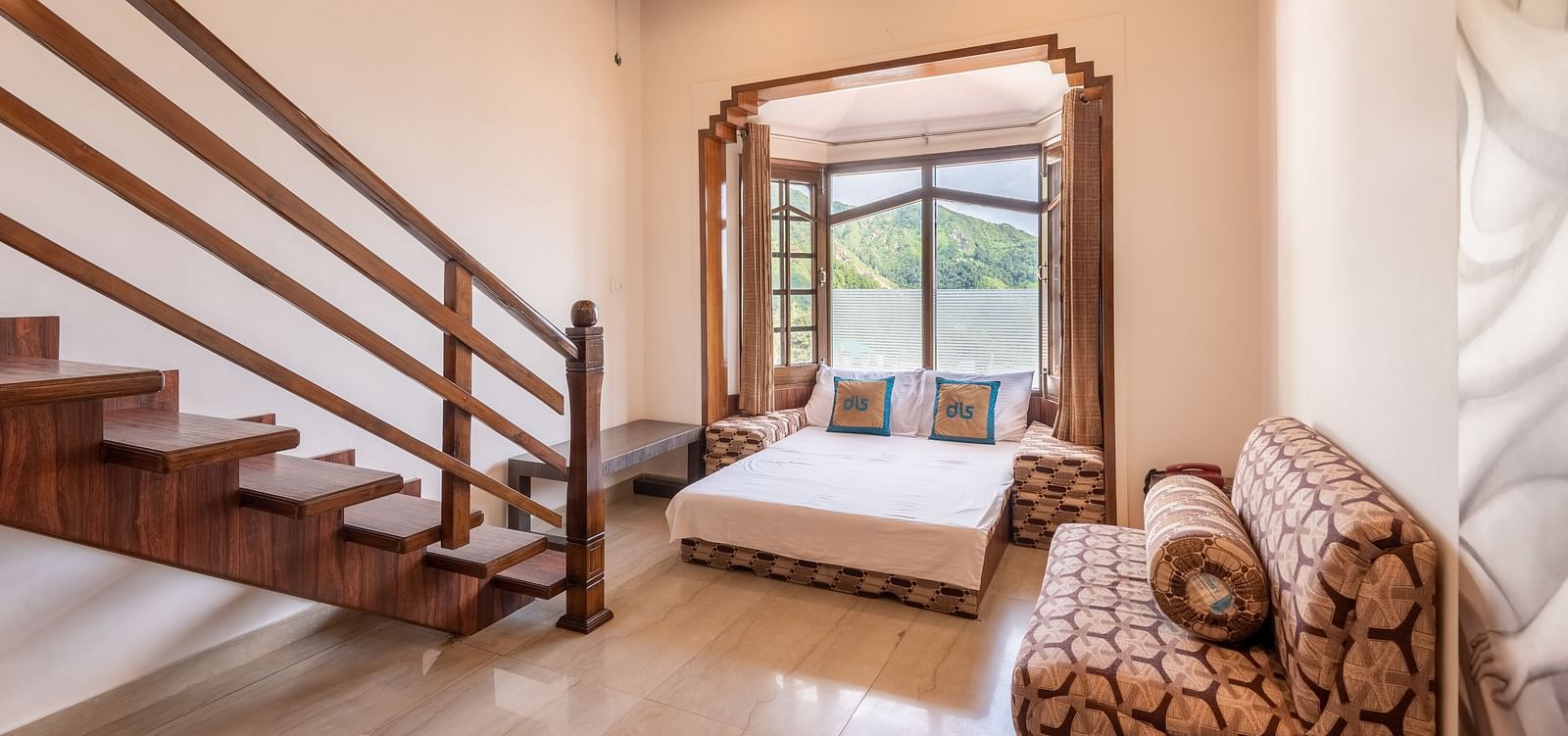 A spacious room near Bhagsunag Temple featuring a wooden staircase, a bed, a sofa, and a large window offering a mountain view – DLS Meghavan Resort.